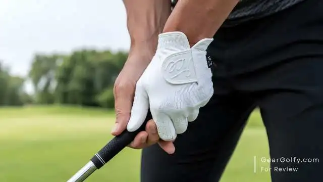 A golfers stands on a green field, gripping a golf club, ready to take a swing.